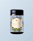 A jar labeled "Flower Powder: Butterfly Bergamot Matcha" displays blue and green botanical illustrations on a light blue background, emphasizing the elegance of organic ceremonial matcha.