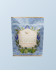 A blue floral pouch labeled "Flower Powder: Butterfly Bergamot Matcha," with gold accents, contains 4.4 oz (125g) of matcha green tea and is set against a light blue background.