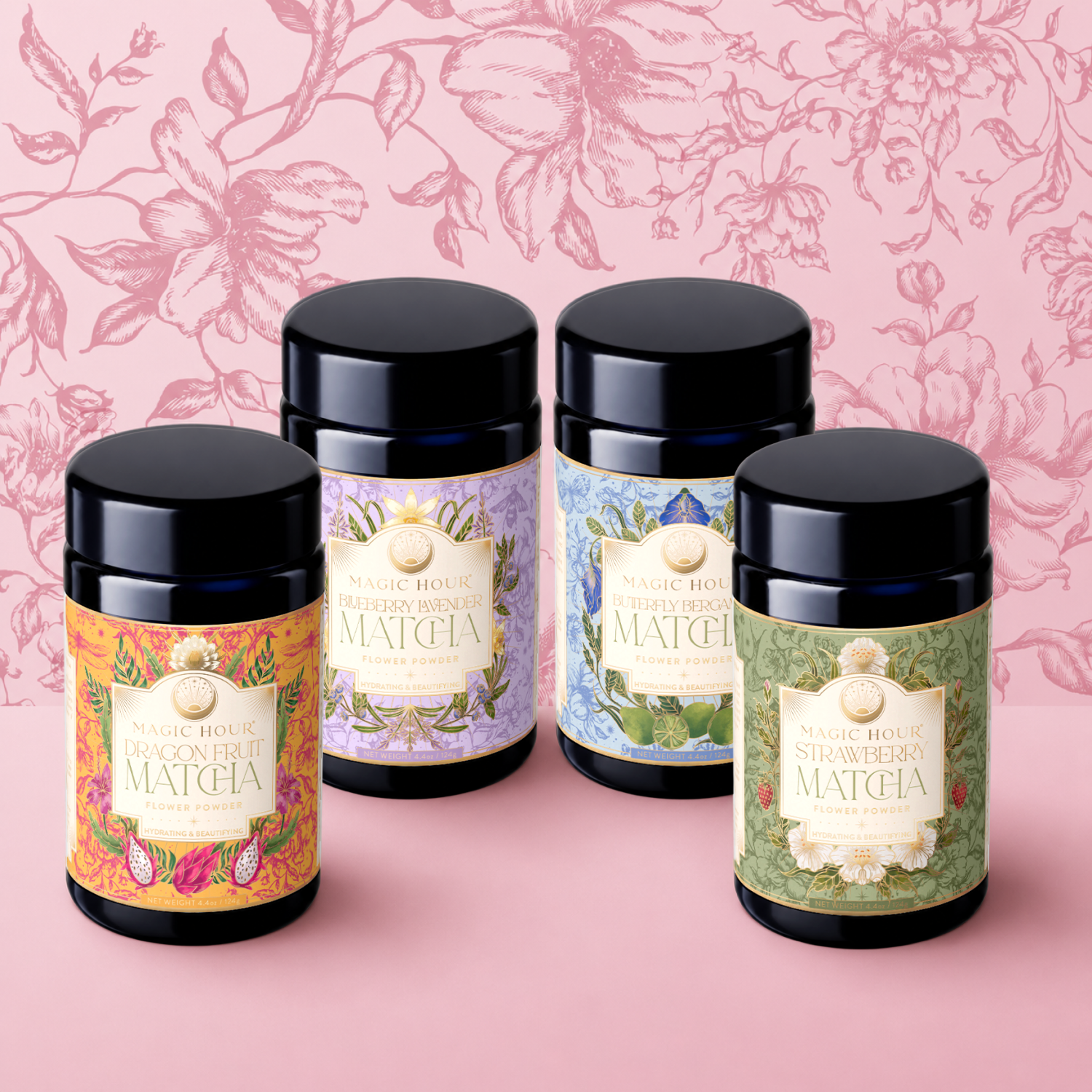 Four cylindrical tea canisters from the "Flower Powder: Matcha Bundle" by Magic Hour—featuring floral designs for Dragon Fruit, Blueberry Lavender Matcha, Elderberry Rose, and Strawberry Matcha—are arranged against a pink floral background and surface.