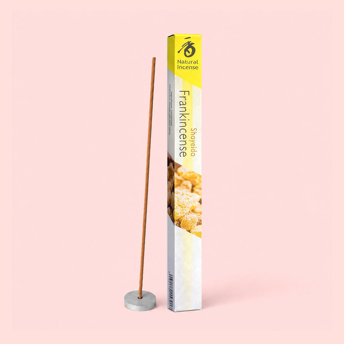 A box of Natural Incense : Frankincense, derived from desert-dwelling trees, stands upright next to a lit incense stick placed in a small round holder, all set against a pale pink background. The blissful fragrance gently fills the air, evoking tranquility and calm.