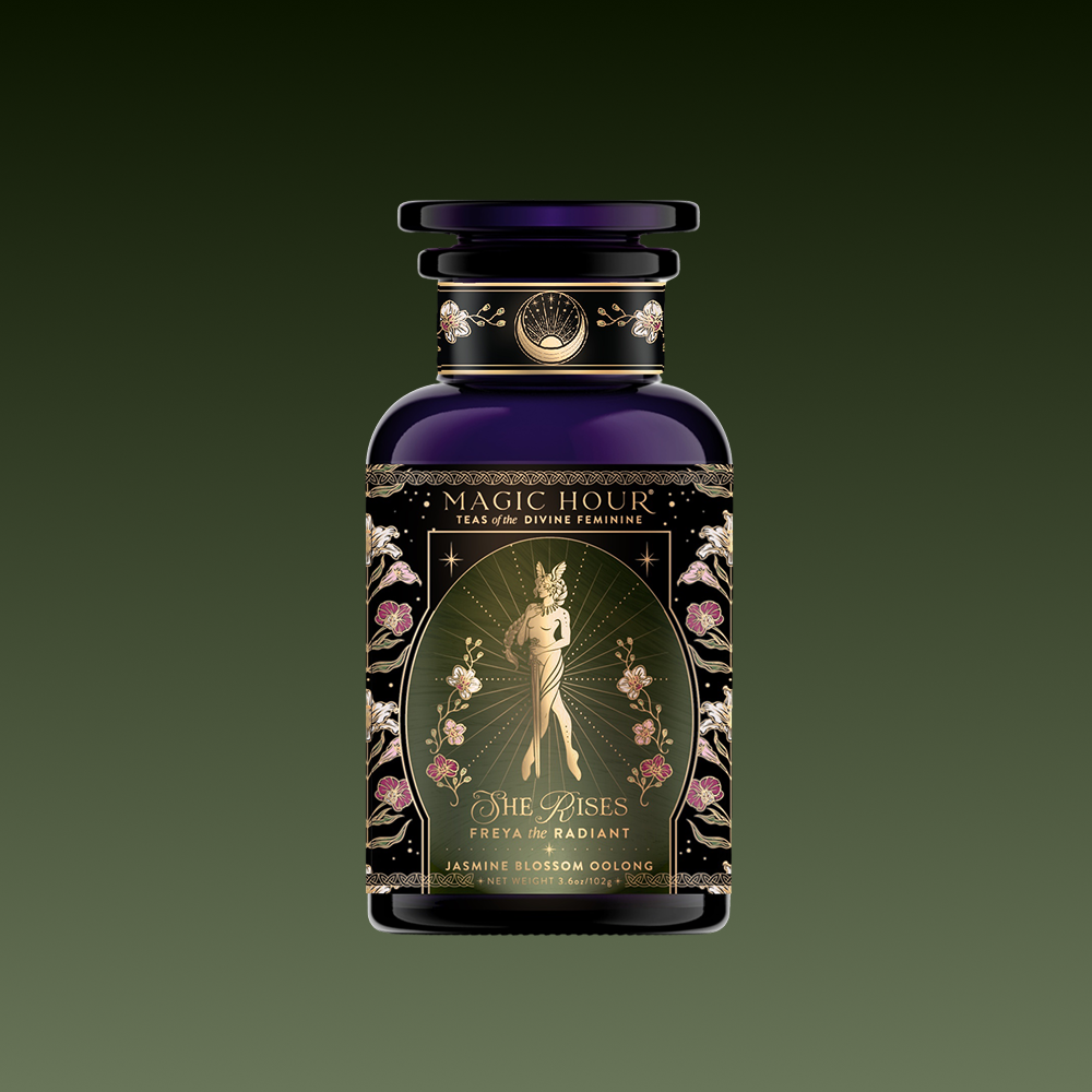 A decorative dark glass tea jar labeled "Freya: The Radiant." The label shows an elegant glowing woman amid flowers with ornate gold designs.