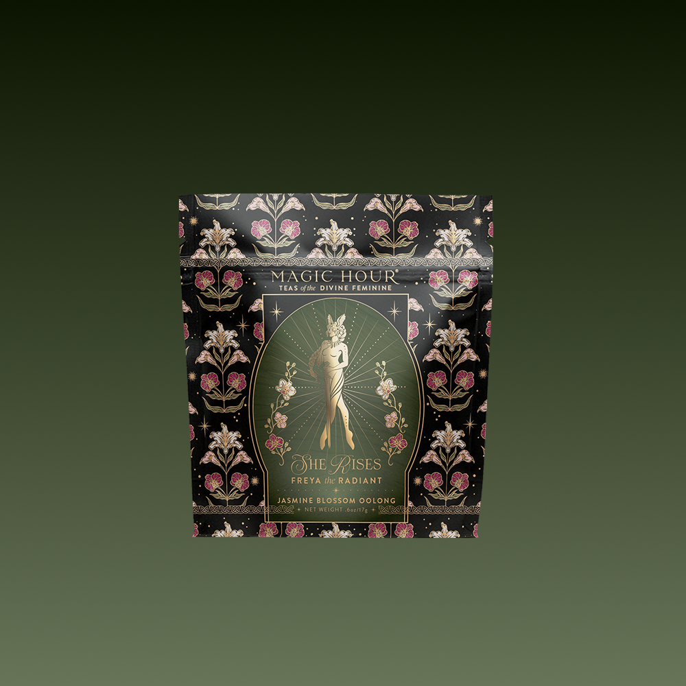 The "Freya: The Radiant" tea comes in a decorative black and gold package with ornate floral designs and a woman among flowers, inspired by the essence of Freya Goddess Tea.
