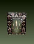 The "Freya: The Radiant" tea comes in a decorative black and gold package with ornate floral designs and a woman among flowers, inspired by the essence of Freya Goddess Tea.