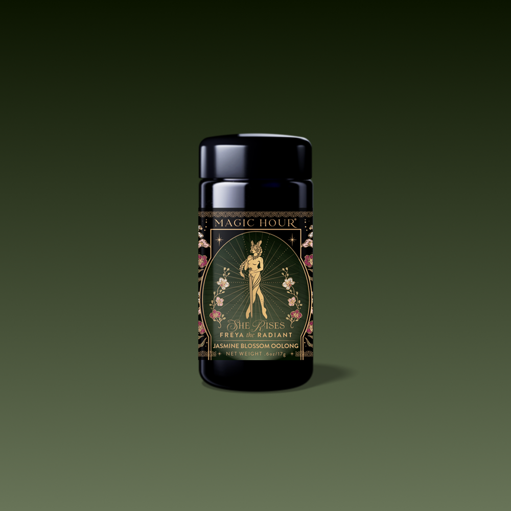 A black tea canister labeled "Magic Hour" features a gold and floral design with an illustrated woman holding flowers. The label reads "Freya: The Radiant Goddess Tea Radiant Jasmine Blossom Oolong" on a dark green gradient background.