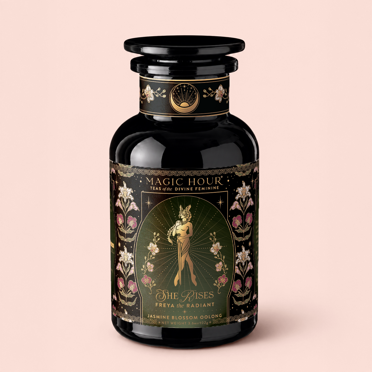 A black tea canister labeled “Magic Hour” features floral designs and an illustration of a woman. The tea, called “Freya The Radiant: Jasmine Bai Hao Oolong with Bergamot &amp; Berry,” offers a fragrant blend inspired by the delicate notes of Oriental Beauty Oolong (Dong Fang Mei Ren).