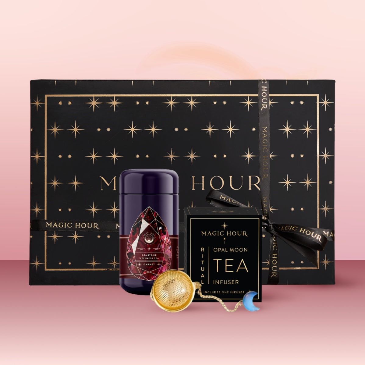 The Garnet January Birthstone Mini Gift Set includes a black box with gold stars, a purple tea canister, an "Opal Moon Tea Infuser" box, and a gold tea infuser with turquoise charm, all displayed on a pink surface.