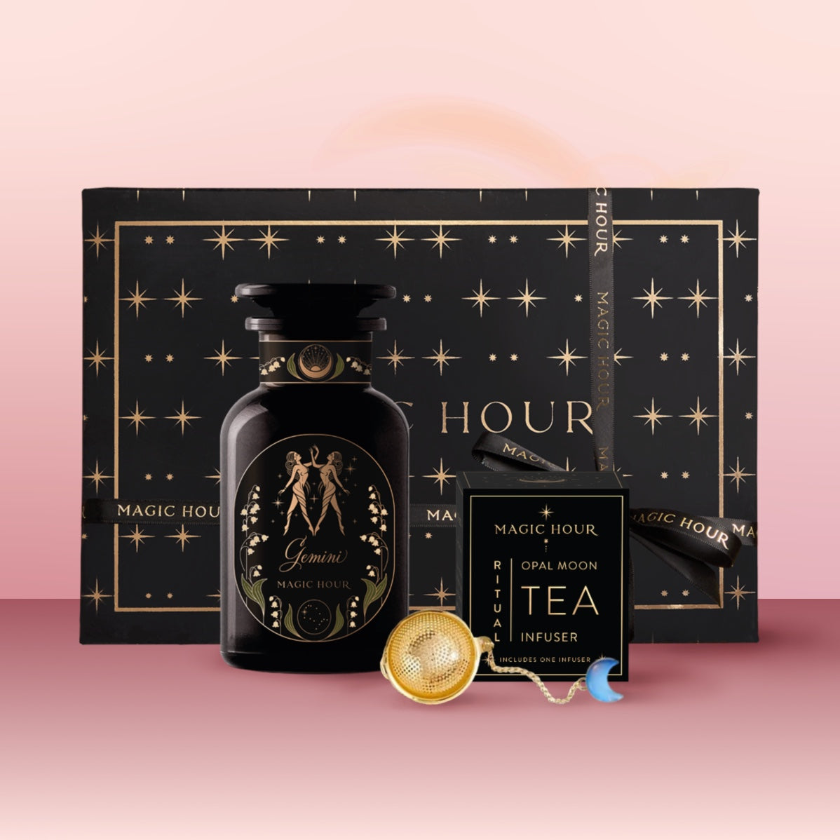 The Gemini Astrology Tea Gift Set includes a black and gold "Magic Hour" box, matching "Gemini" tea jar, tea infuser, and "Opal Moon Ritual Tea" sachet, elegantly arranged on a pink gradient background.