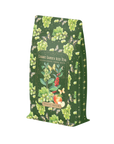 A green package of Green Grape Yerba Mate: Cosmic Garden Iced Tea from Magic Hour. The design features illustrations of green grapes, honeybees, and apple slices on a dark green background, giving it a natural and whimsical look. Enjoy this delightful organic tea in loose leaf form.