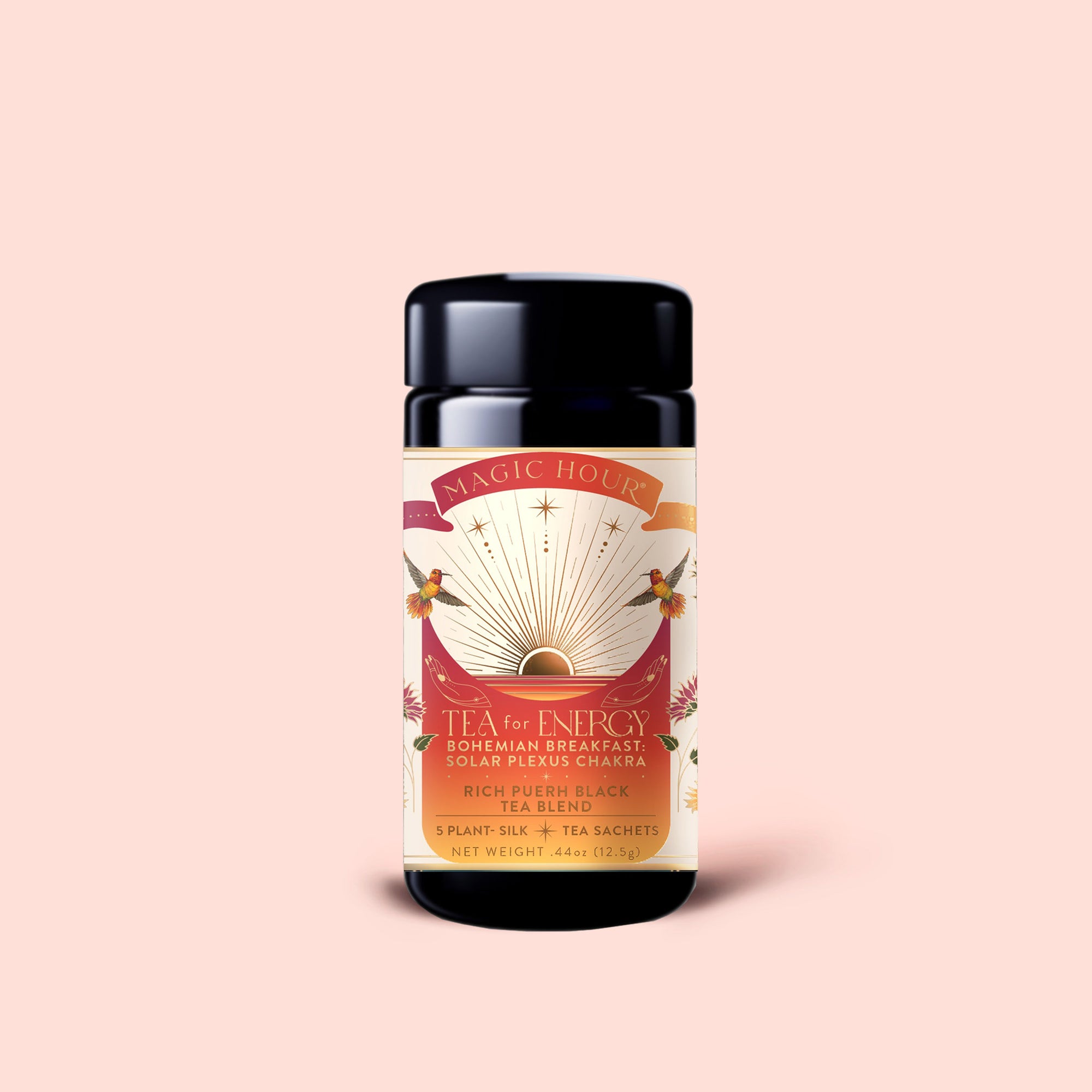 A cylindrical container of Magic Hour's "Tea for Energy: Bohemian Breakfast: Rich Puerh Black Tea Blend," featuring a sunburst design, pink and gold accents, and floral details, is set against a pale pink background—this organic puerh tea blend is known to support energy and digestion.