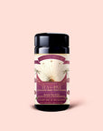 A jar of Tea for Love: Soulmate: Black Tea with Chocolate & Raspberries rests on a light pink background. This Fair Trade blend combines rich chocolate, vibrant raspberries, and delicate rose petals. Its label is adorned with a sunburst, roses, and palm leaves accented in gold.