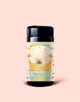 A canister of "Tea for Beauty: Renewal: Peach, Goji & Rose Oolong Tea" sits on a peach background. The label displays a sunrise, flowers, and lists ingredients such as Goji Berries, Peach Oolong Tea, rose, Ti Quan Yin Oolong, along with “5 plant silk tea sachets.”.