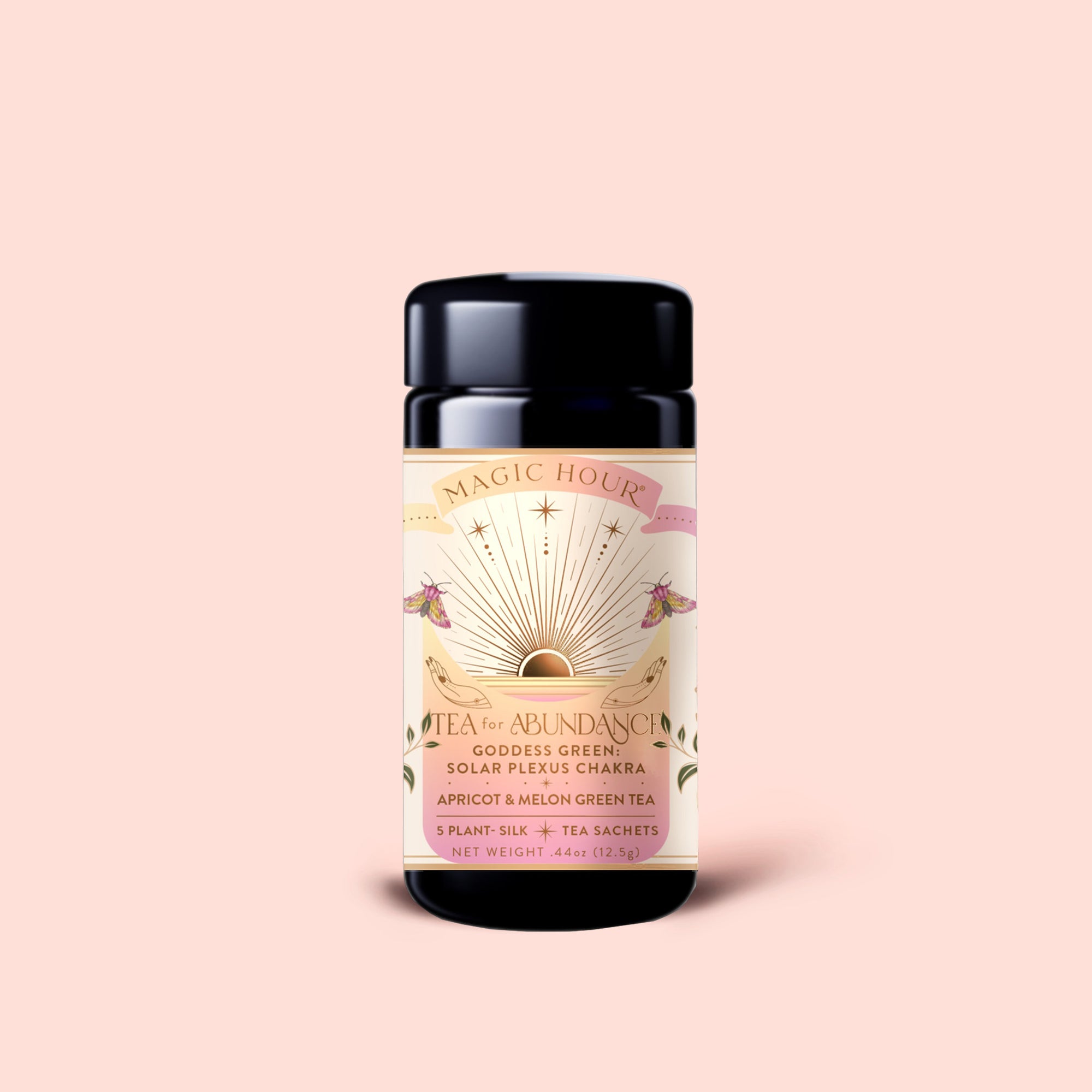 A black tea canister labeled “Tea for Abundance: Goddess Green: Apricot &amp; Lychee Green Tea,” adorned with sun and floral designs on a peach background. This blend features apricot and lychee green tea artfully combined with organic lemongrass, crafted to nourish the solar plexus chakra.