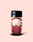 A container of Magic Hour "Tea for Manifesting: Ruby Moon" herbal tea, featuring hibiscus, elderberry, and passionfruit, adorned with sunburst celestial artwork and pink floral details on a light pink background.