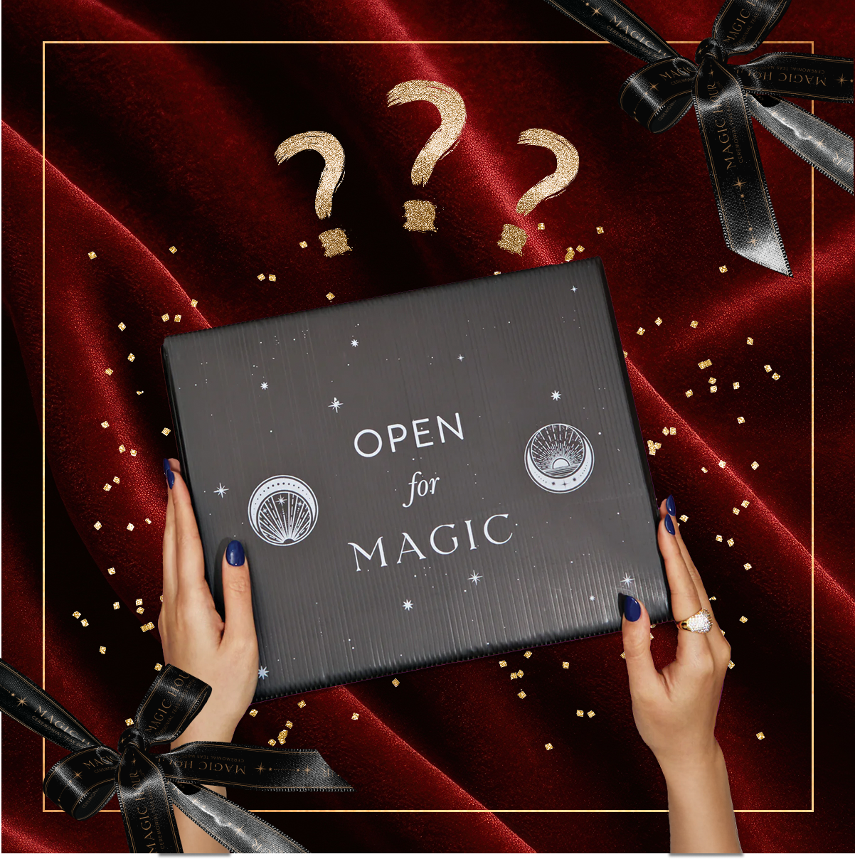 A person with dark blue nails holds the Black Friday Mystery Box labeled "OPEN for MAGIC" above red velvet, gold confetti, and black ribbons, with three gold question marks overhead—suggesting premium teas or tea accessories inside.