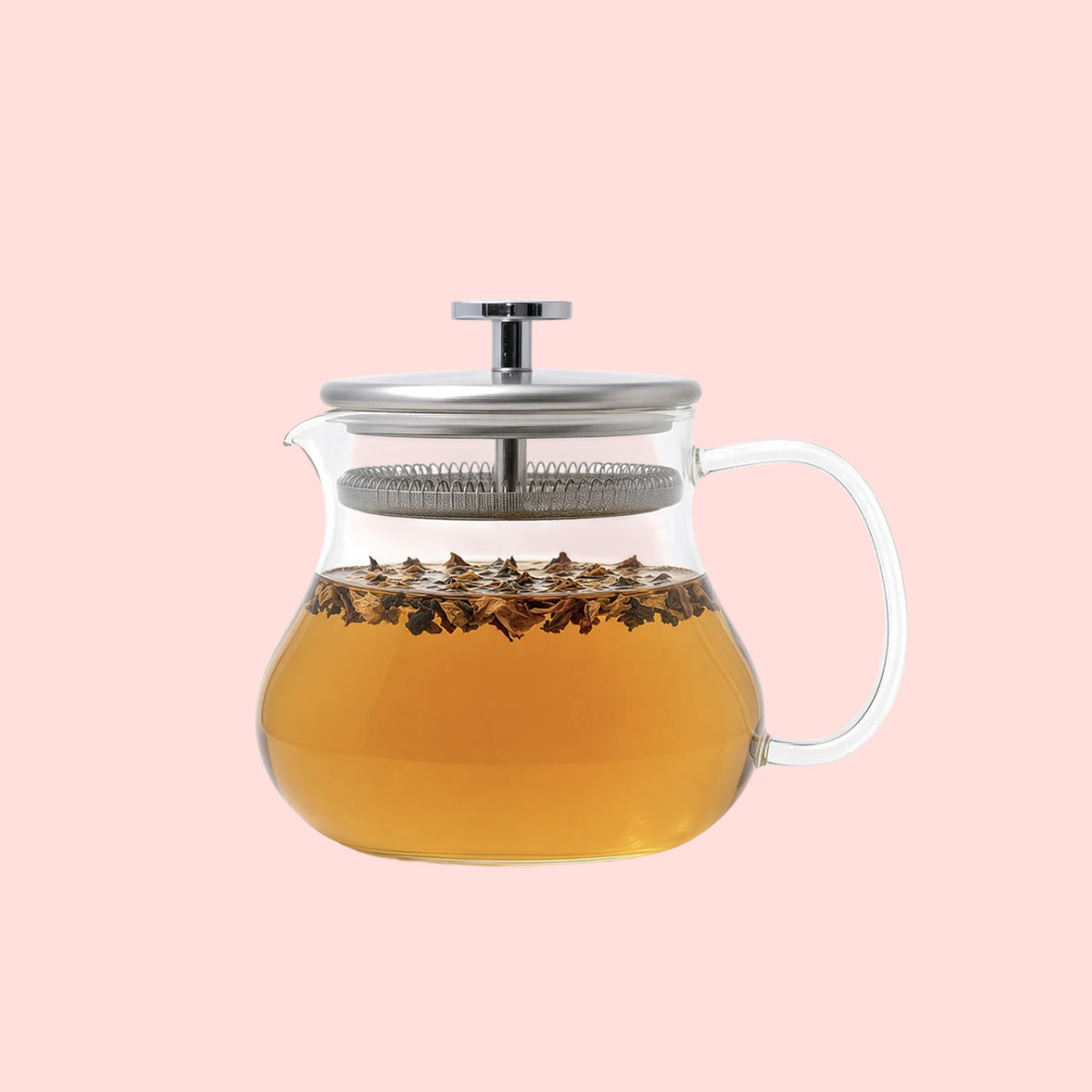 The Essential Perfection Teapot with Built-in Strainer, made from borosilicate glass and featuring a metal lid, is filled with light brown tea and loose tea leaves and set against a pale pink background.