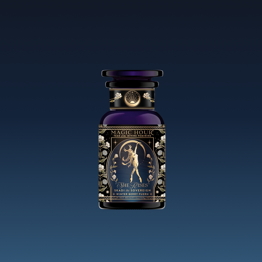 A dark royal blue perfume bottle labeled "Skadi The Sovereign - Winter Berry Puerh" features gold accents, a mythic archer illustration, and intricate floral designs, inspired by a berry-infused puerh tea ceremonial blend.