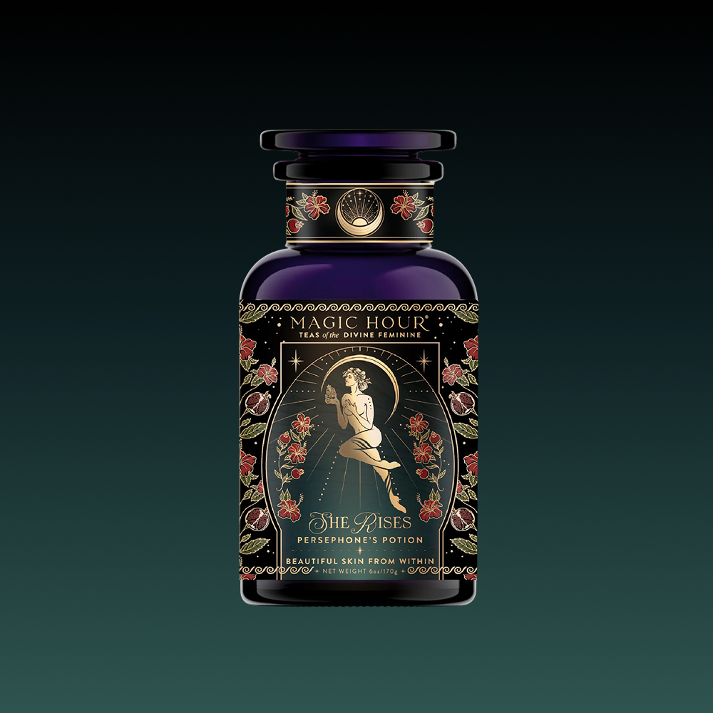 A dark, ornate bottle from the Monthly Magic Tea Subscription Box labeled "Magic Hour, Persephone’s Potion," features a woman amid roses and gold stars, celestial designs, “She Rises,” and honors goddess tea rituals.