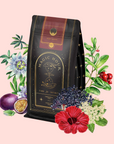 A black and gold bag of Ruby Moon™: Hibiscus Elderberry Tea is surrounded by passionflowers, berries, elderflowers, and green leaves on a light pink background. This caffeine-free blend is rich in vitamin C.