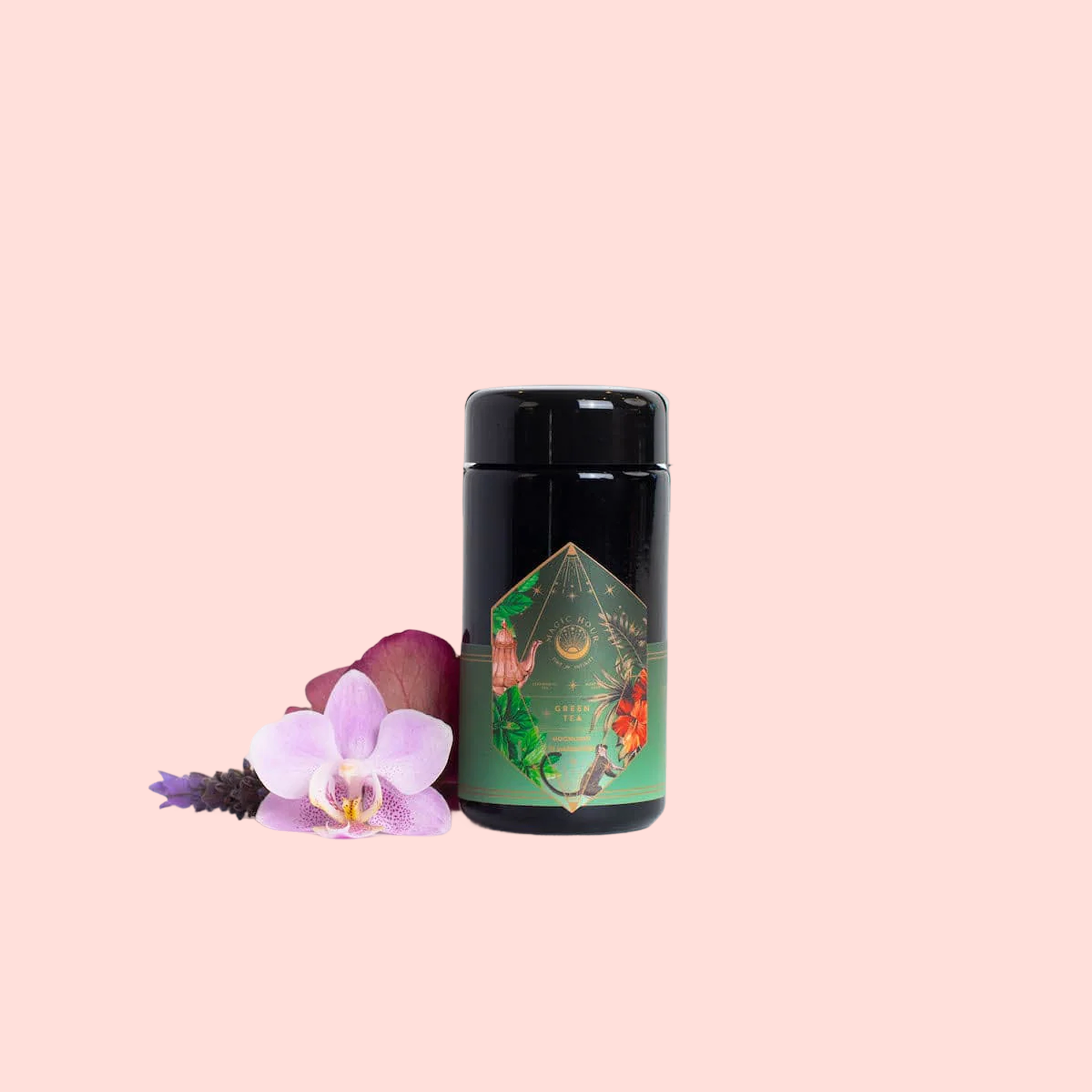 A black jar with a colorful geometric label sits beside a pink orchid, red petal, and lavender on light pink—ideal for storing Moonlight in Marrakesh: Spiced Mint Green Tea.