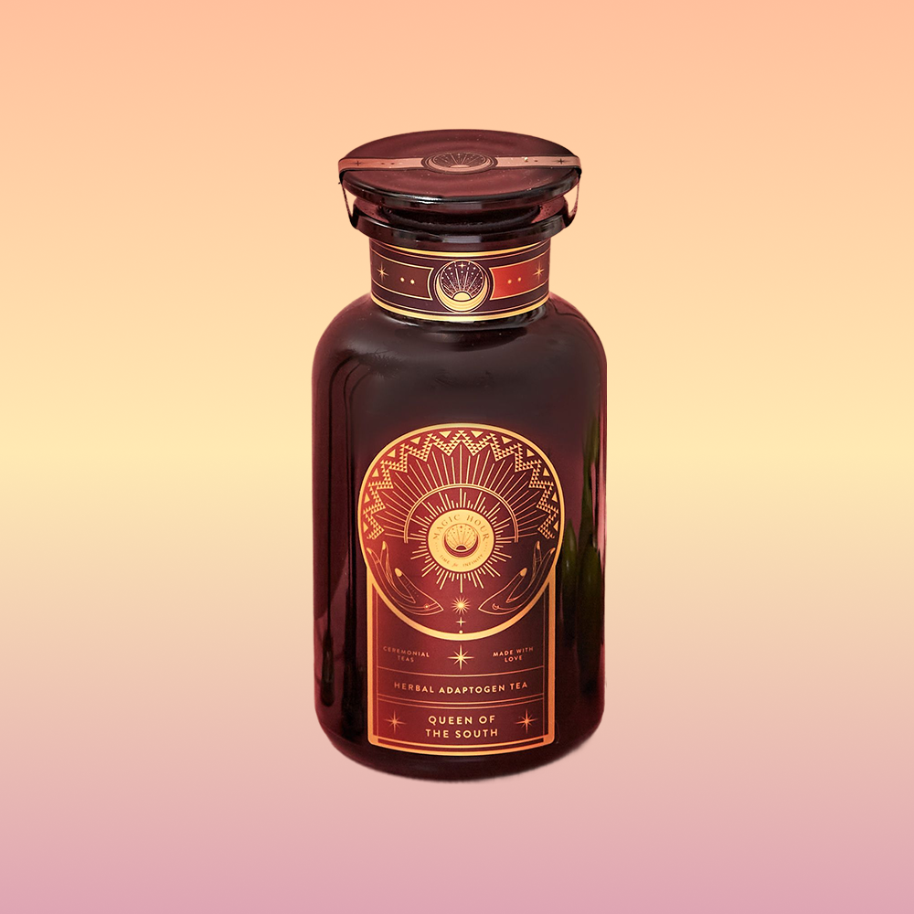 A dark glass bottle with a gold and orange ornate label featuring a sun and geometric designs, labeled "Queen of the South Cocoa Detox Tea," showcases a caffeine-free adaptogenic tea on a warm gradient background.
