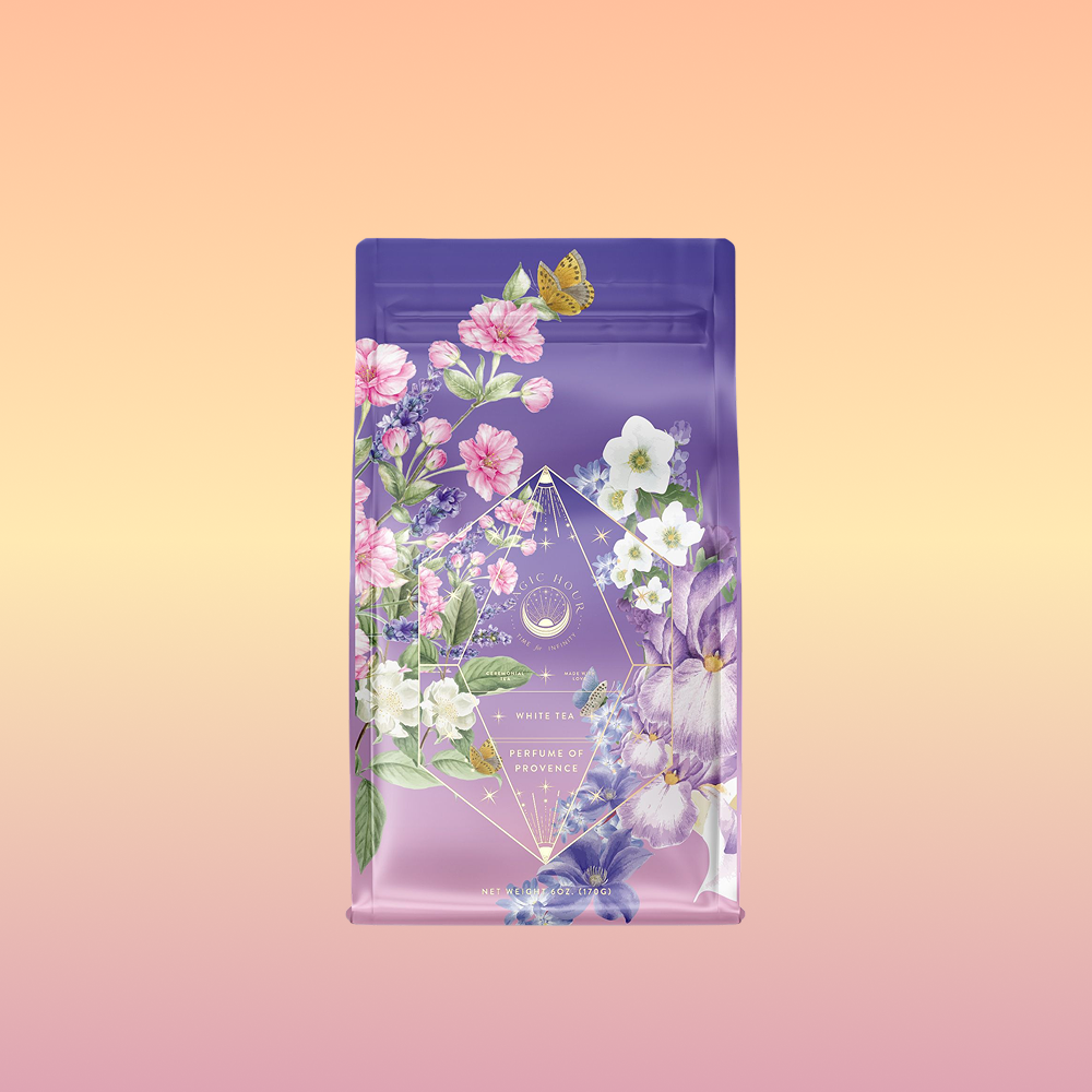 A purple and pink tea package with flowers, leaves, and a yellow butterfly on a peach-yellow gradient. The label reads "Perfumes of Provence: Lavender Bouquet Tea for Calm Moods and Beautiful Skin," suggesting a soothing floral tea.