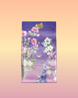 A purple and pink tea package with flowers, leaves, and a yellow butterfly on a peach-yellow gradient. The label reads "Perfumes of Provence: Lavender Bouquet Tea for Calm Moods and Beautiful Skin," suggesting a soothing floral tea.