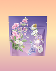 The Perfumes of Provence: Lavender Bouquet Tea for Calm Moods and Beautiful Skin features a lavender-toned pouch with pink, white blossoms, purple irises, and a butterfly on a peach-pink gradient background.