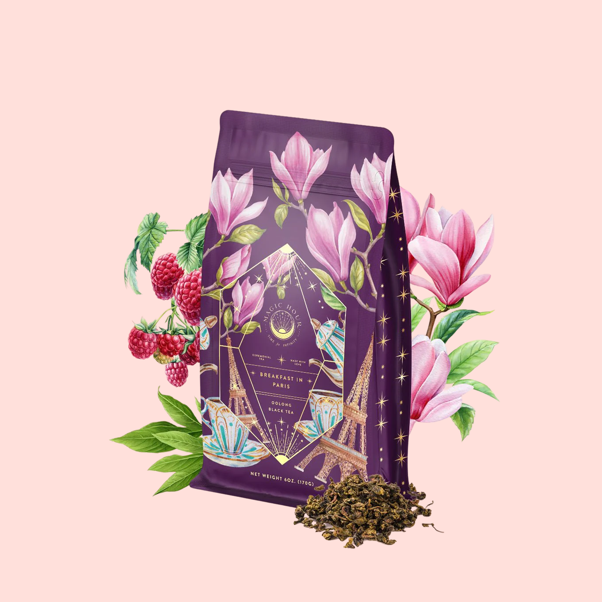 A purple "Breakfast in Paris-Oolong Black Tea Scented with Fruits &amp; Flowers of Secret Parisian Gardens" package, adorned with floral and Paris motifs, is surrounded by magnolias, raspberries, green leaves, and loose tea on a pale pink background.