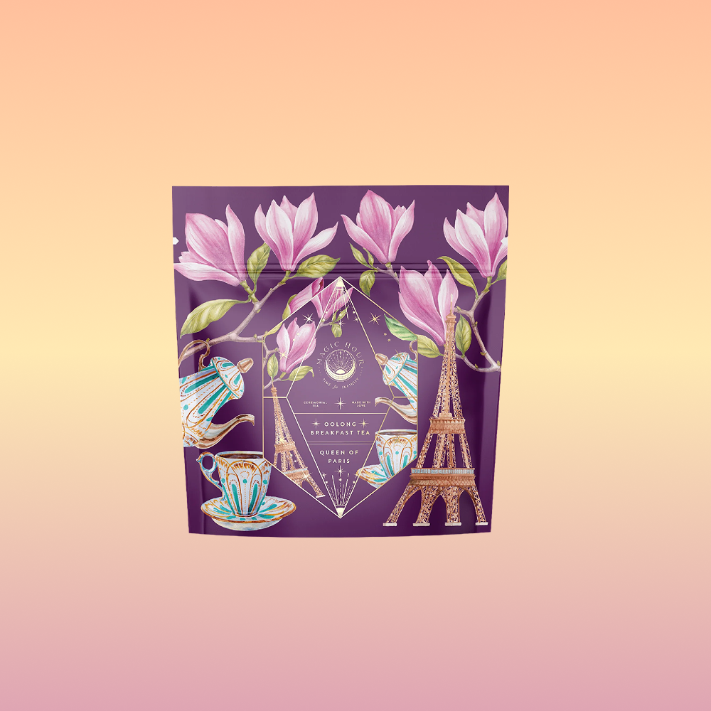 A purple pouch for Breakfast in Paris-Oolong Black Tea, scented with fruits and flowers of secret Parisian gardens, features pink magnolia flowers, teacups, teapots, and the Eiffel Tower on a soft peach-to-pink gradient background.