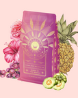 The Queen of the Tropics: Rosé all Day Alternative Tea features a vibrant pink package with gold celestial designs, surrounded by pineapple, hibiscus, grapes, guava, and Garcinia Cambogia on a pale pink background.