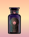 A dark purple glass bottle labeled "Queen of the Rainforest: Cacao-Berry Tea," adorned with gold and pink celestial designs, hints at a vibrant cacao-berry herbal blend—ideal for fans of Guayusa tea—set against a soft pastel gradient background.