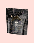 A black and purple resealable tea pouch labeled "Goddess of Earl: Lavender London Fog—Tea for Blooming Clarity & Calm Moods" features celestial illustrations and bergamot notes, displayed on a pale pink background.