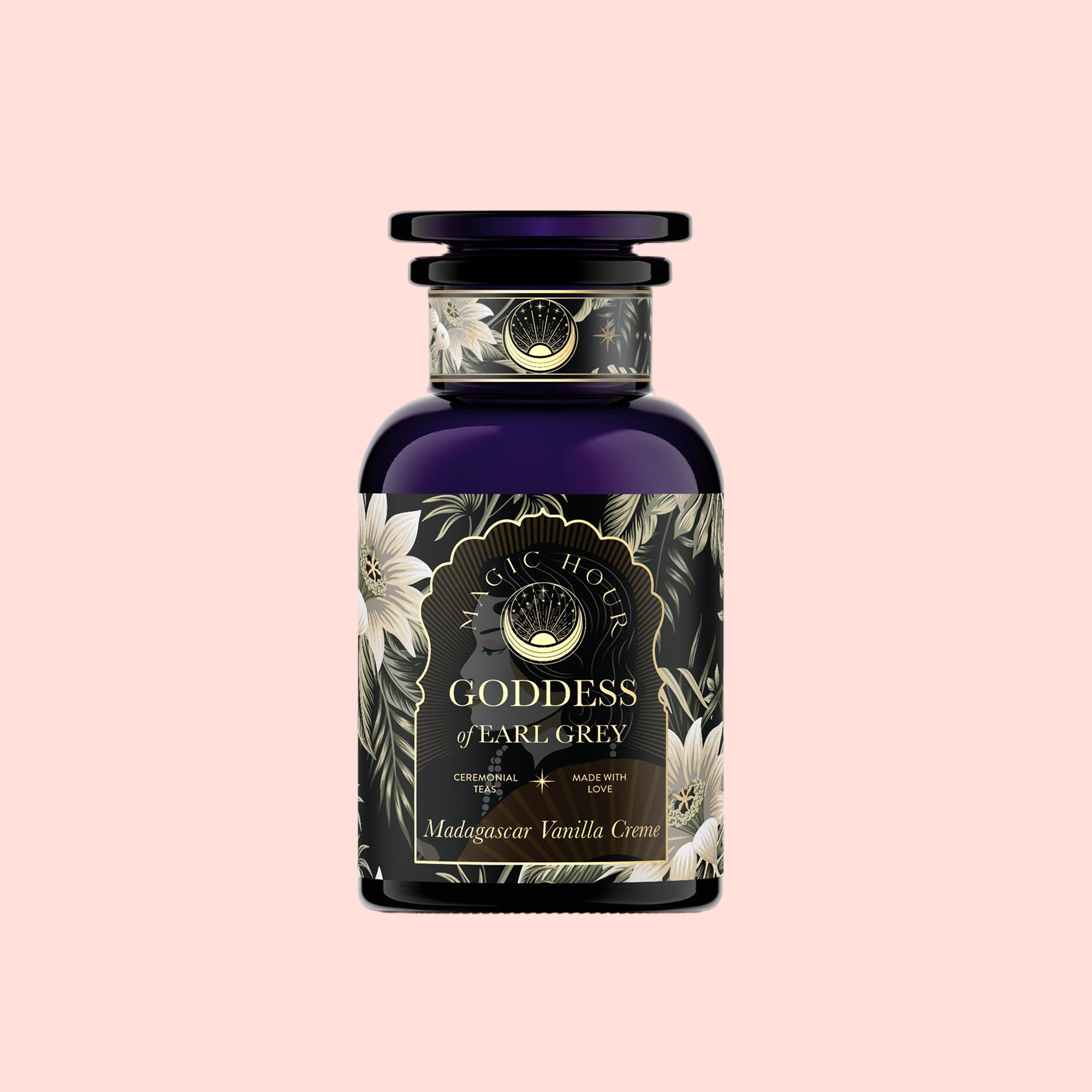 A dark glass bottle labeled "Goddess of Earl: Madagascar Vanilla Creme Tea for Soothing Delight &amp; Delicious Decadence" with floral and gold accents, set against a pale pink background.