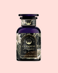 A dark glass bottle labeled "Goddess of Earl: Madagascar Vanilla Creme Tea for Soothing Delight & Delicious Decadence" with floral and gold accents, set against a pale pink background.