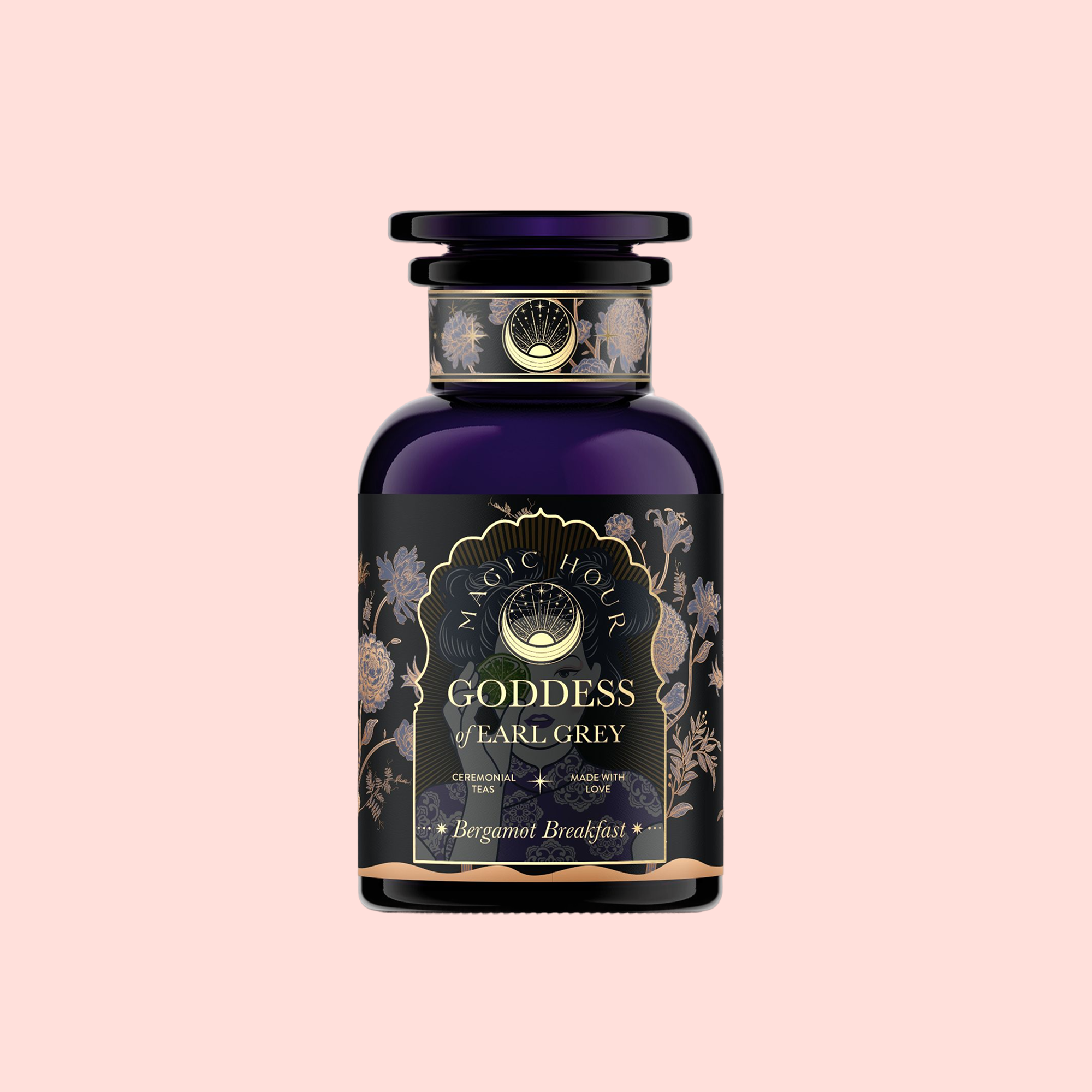 A dark blue glass jar with an ornate black and gold label reading "Goddess of Earl: Lady Luck Oriental Beauty Oolong Tea" sits against a light pink background, its elegant floral design hinting at tea notes of bergamot, grapefruit, and loose leaf oolong.