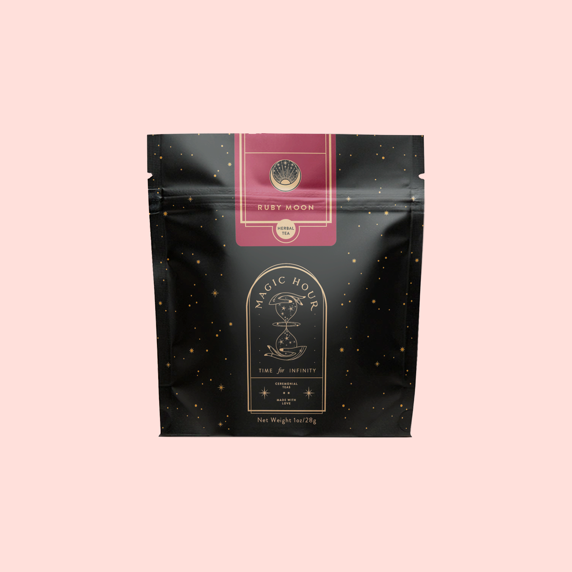A black and gold pouch labeled "Magic Hour" with a celestial design and "Ruby Moon™ : Hibiscus Elderberry Tea" on a light pink background. The caffeine-free tea packaging has small gold dots and a decorative emblem at the top.
