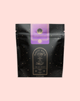 A black resealable tea bag with gold stars and a purple label reading "Lucid Dreams: Tulsi-Turmeric Herbal Tea for Sleep & Calm." The "Magic Hour" branding and celestial design make it perfect for enjoying soothing caffeine-free chai.