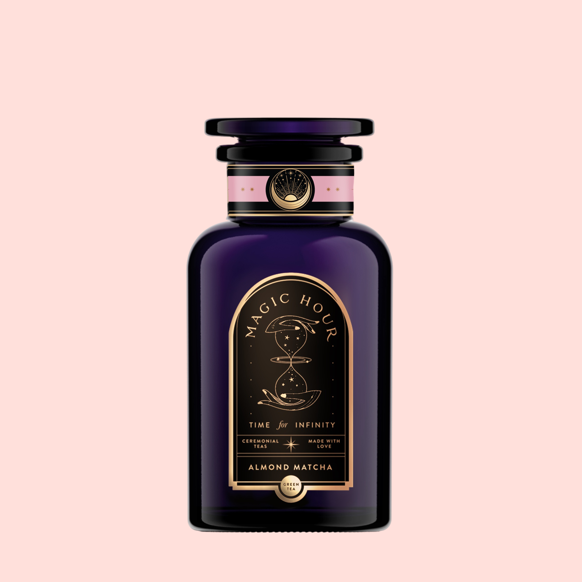 A sleek dark purple glass bottle with a black cap holds "Almond Matcha Green Tea for Joy." The black and gold label features pink and gold accents, set against a pale pink background.