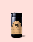 A black tea jar labeled "Bohemian Breakfast Vanilla Puerh Black Tea for Digestion & Energy" with a gold label sits on a light pink background. The 1 oz (28g) jar is a perfect coffee alternative.