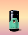 A black jar labeled “Mantra Mint™ Herbal Tea” with a mint green label sits on a soft peach, yellow, and pink gradient background. This caffeine-free blend features Ashwagandha and has a dark glossy lid with a subtle shadow beneath.