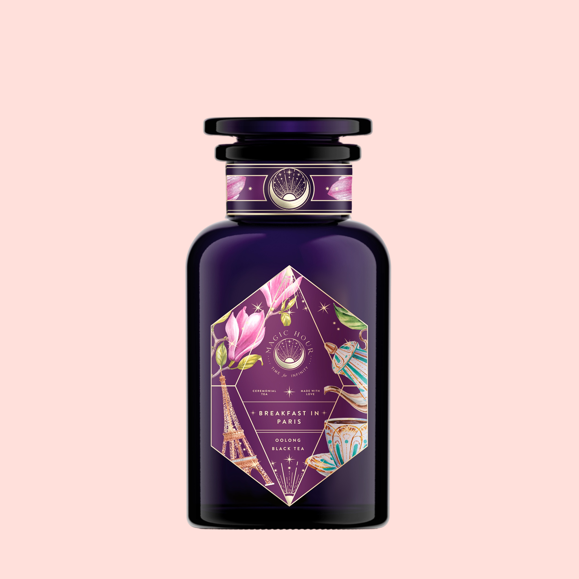 A dark purple canister labeled “Breakfast in Paris—Oolong Black Tea Scented with Fruits &amp; Flowers of Secret Parisian Gardens” features gold and pink accents, floral designs, the Eiffel Tower, and a butterfly on a pale blush background.