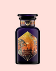 A dark purple perfume bottle with a geometric orange label depicting tropical plants, a monkey, birds, and a sunrise evokes Bali Bliss: Coconut-Lime & Ginger-Melon White Tea—set against a pale pink background. The label reads “Bali Breakfast.”.