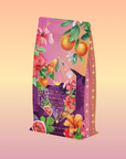 Pink Moment Pixie - Hibiscus Tangerine Dream Herbal Tea comes in a vibrant package featuring oranges, hibiscus flowers, figs, and grapes on a pink-purple background with glowing stars—ideal for caffeine-free or tangerine hibiscus tea fans.
