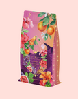 The Pink Moment Pixie - Hibiscus Tangerine Dream Herbal Tea features a vibrant pink and purple package with geometric label, decorated with colorful illustrations of oranges, hibiscus flowers, grapes, and immune-supporting elderberry. Caffeine free.