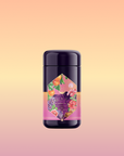 A dark purple cylindrical container of Pink Moment Pixie - Hibiscus Tangerine Dream Herbal Tea, with a colorful label showing oranges, grapes, flowers, and elderberry, set on a soft peach and yellow gradient background.