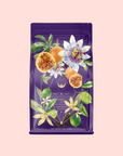 A purple tea bag with illustrated passion fruit, leaves, and flowers features gold accents and text: "Romance in Ravello - Chocolate-Passionfruit-Rose-Cream White Tea" on a light pink background.