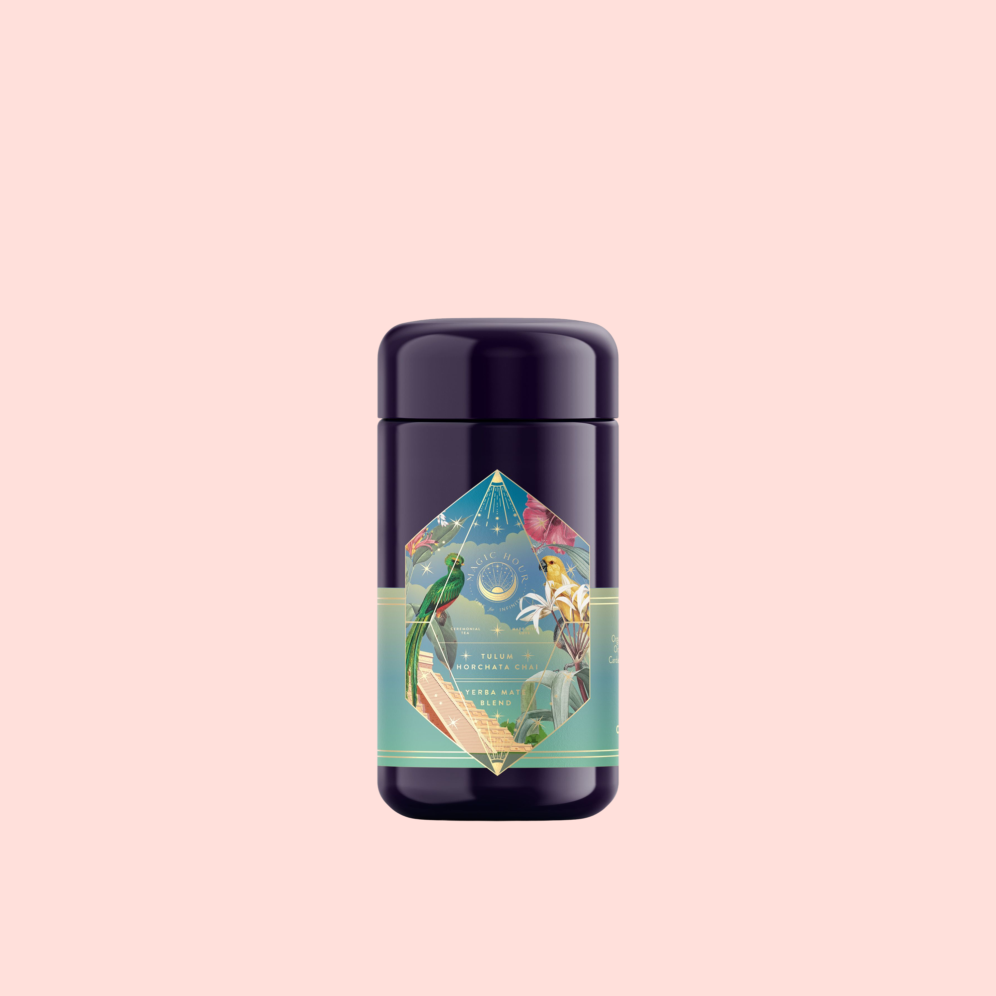 A dark, cylindrical container with a colorful label featuring birds and plants sits against a plain light pink background—inside is Tulum Horchata Chai, an energizing yerba mate and ashwagandha adaptogenic wellness potion.