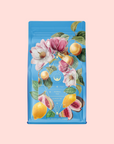 A blue tea packet with floral and fruit illustrations, including magnolia, figs, and green leaves. The label reads "Herbal Tea, Summer in Amalfi," featuring Mediterranean notes and organic lemon peel.
