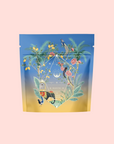 Sri Lankan Sunrise features a vibrant tea package with palm leaves, roses, lemons, and birds on a gradient blue-to-yellow background. It presents organic black tea inspired by Sri Lankan breakfast blends against a pale pink backdrop.
