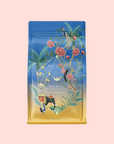 A vibrant tea bag with blue and gold gradient packaging, adorned with illustrated flowers, leaves, and birds. The geometric central label reads "Sri Lankan Sunrise," inspired by organic black tea and Ceylon cinnamon.